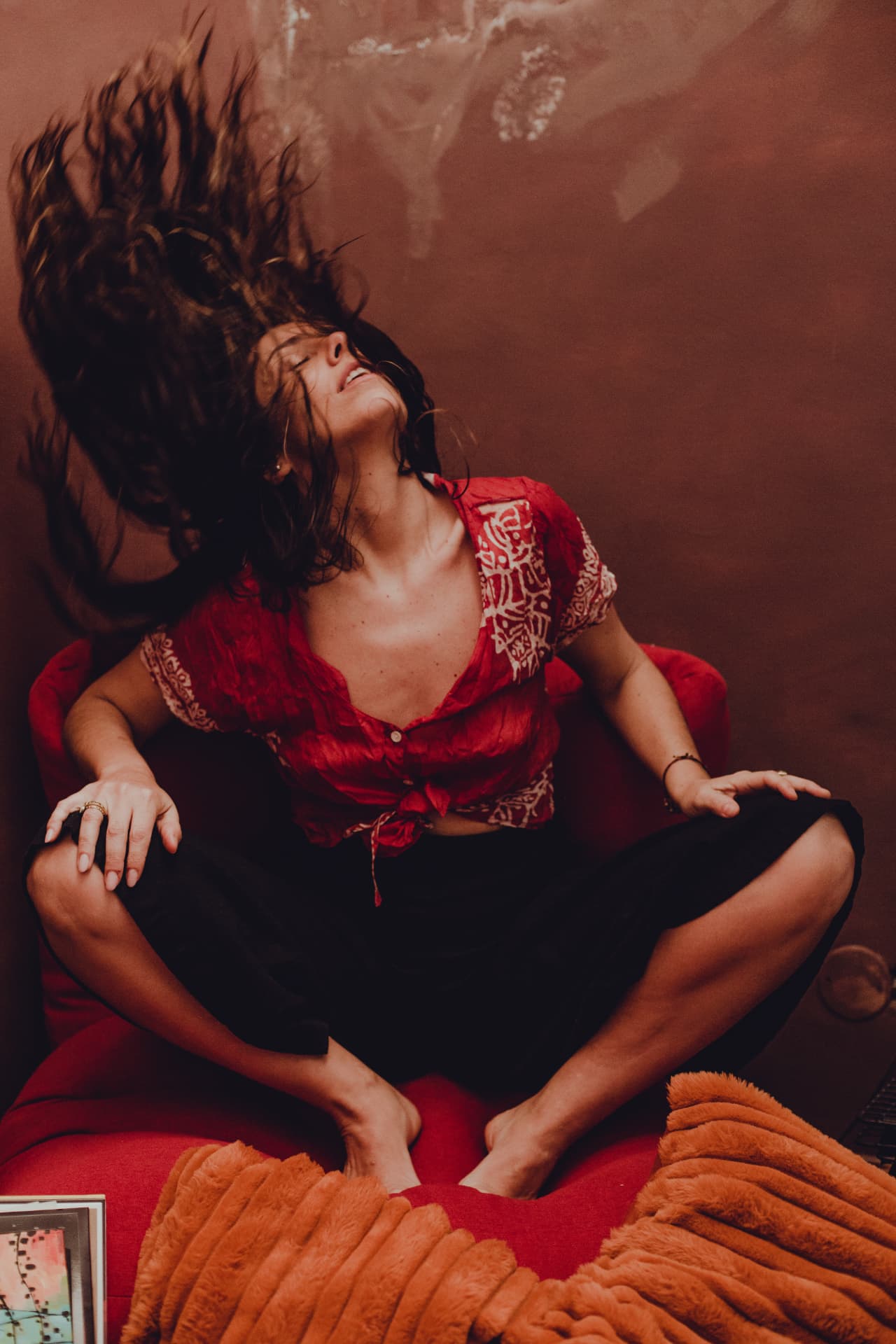 Carolina Zingler em pose dinâmica, cabelo ao vento, sobre sofá vermelho